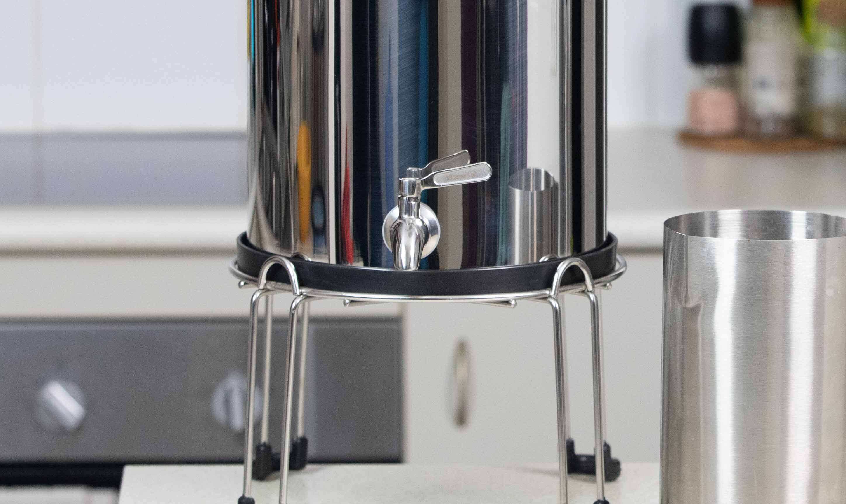 Filteroo® Superoo stainless steel gravity water filter on a stand featuring the stainless steel tap and jug in a kitchen setting.