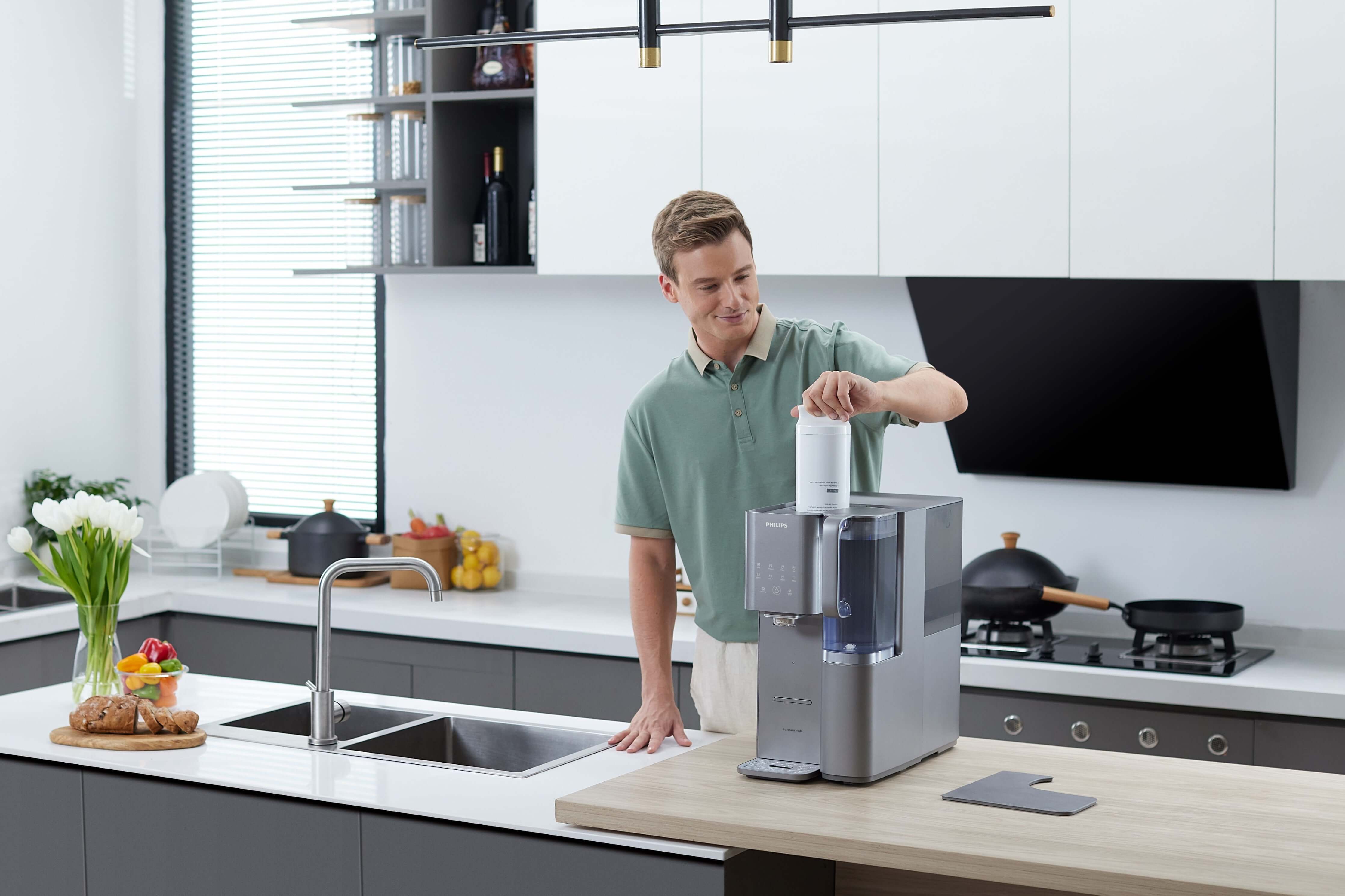 A person operates a Philips Aquaporin Inside Reverse Osmosis Filter ADD583/79 in a large, modern kitchen complete with a sink and various kitchen items nearby.