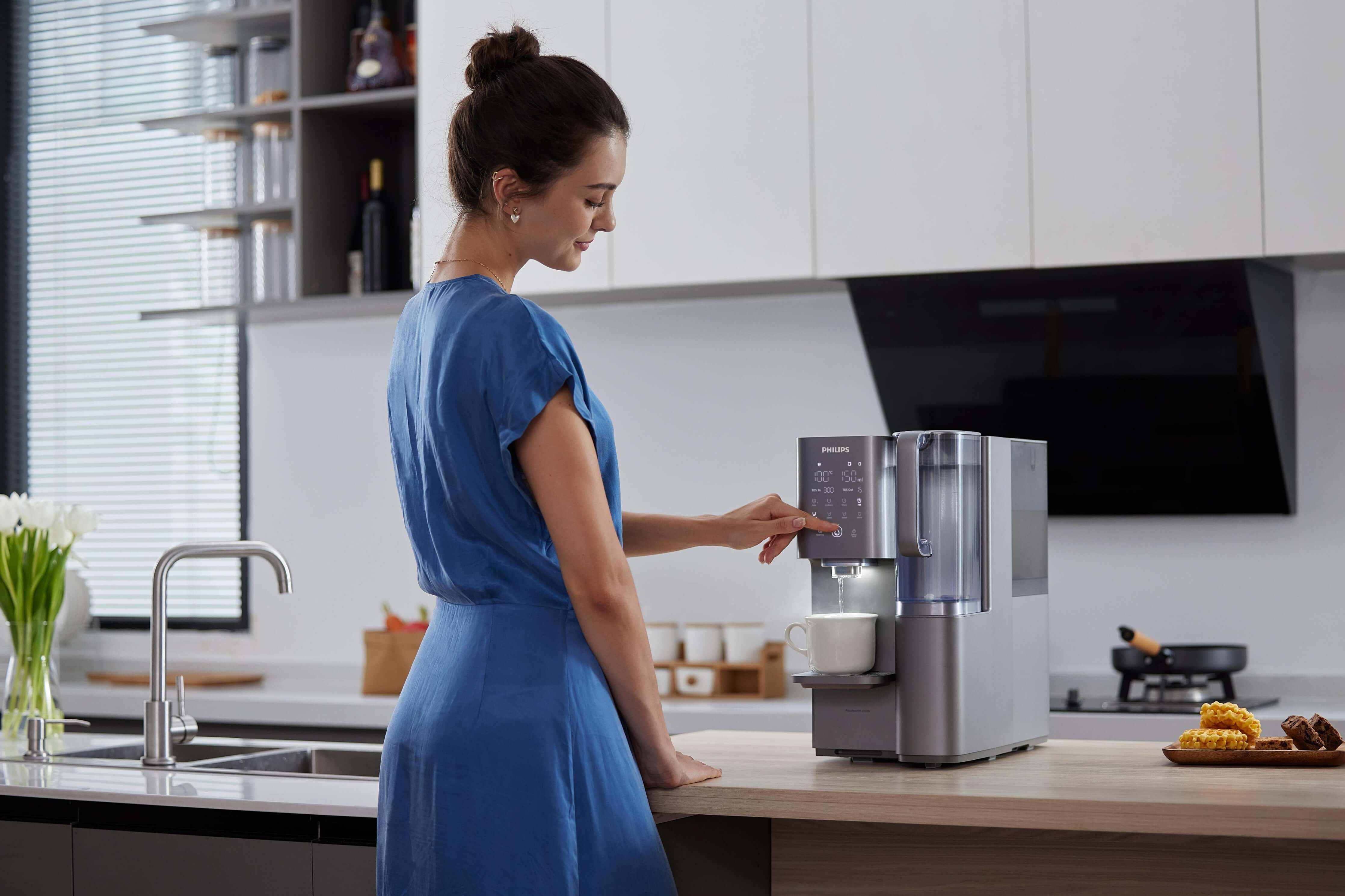Woman using Philips Aquaporin Reverse Osmosis Water Station in kitchen.