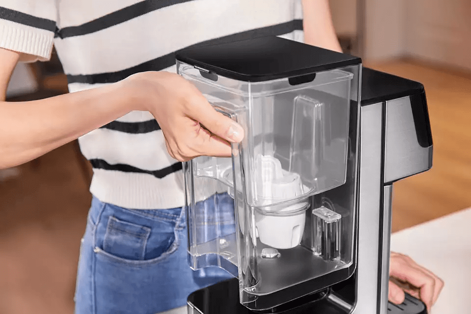 An individual is operating the Philips Compact Water Station ADD5910M/79, adjusting its transparent water container that features Micro X-Clean Filtration for optimal results.