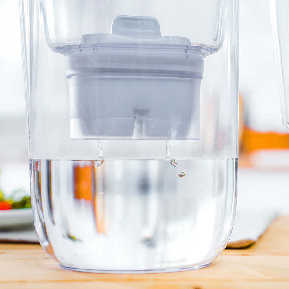 Close-up of water being filtered through the Philips Micro X-Clean Carbon Filter AWP211 for MF Water Station, with droplets falling into a clear pitcher.