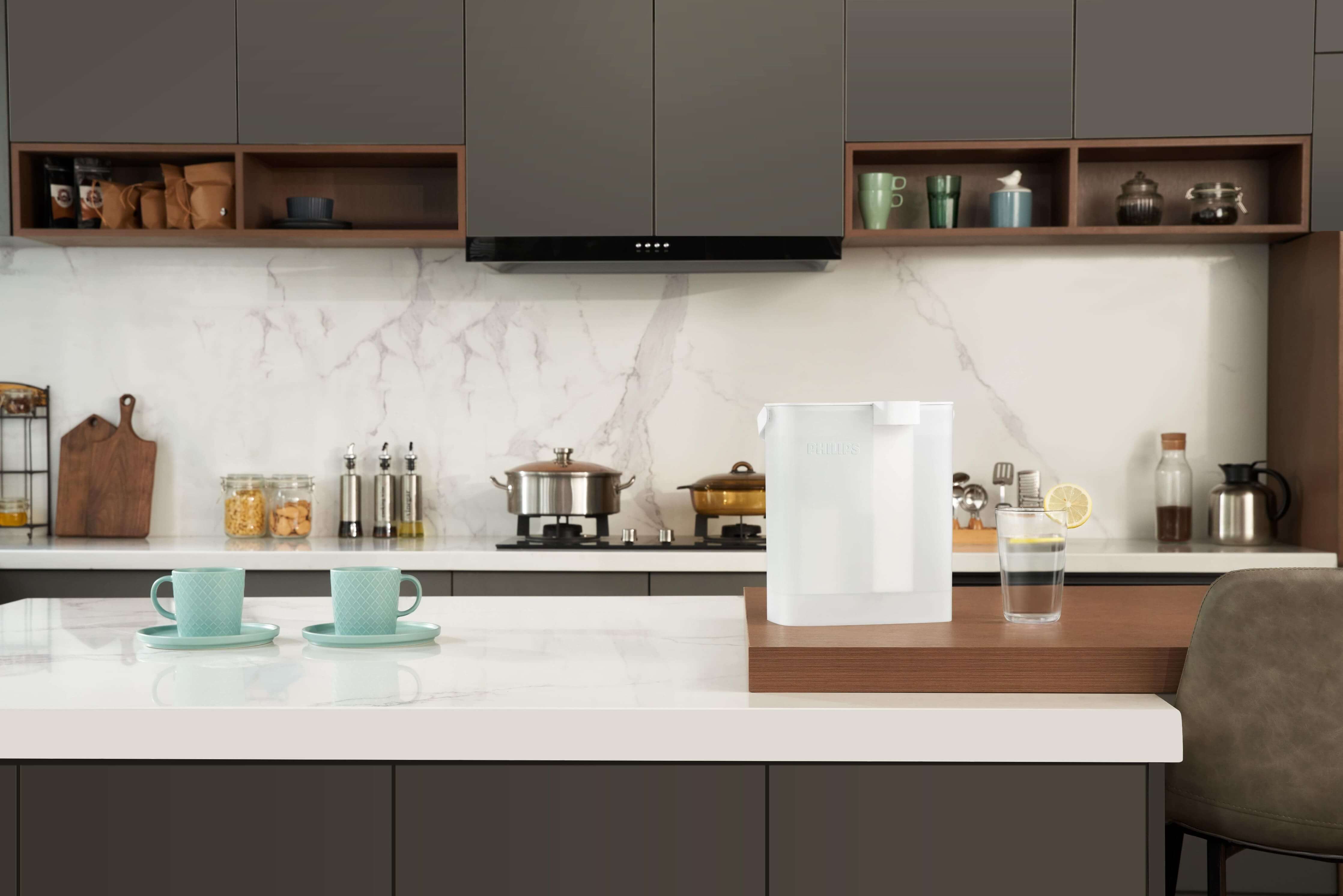 A modern kitchen showcases a marble backsplash, cooking pots, mint cups on the countertop, and a water pitcher featuring the Philips Next-generation instant water filter AWP2980WH with Micro X-Clean instant filtration technology, complete with a lemon slice for instant refreshment.
