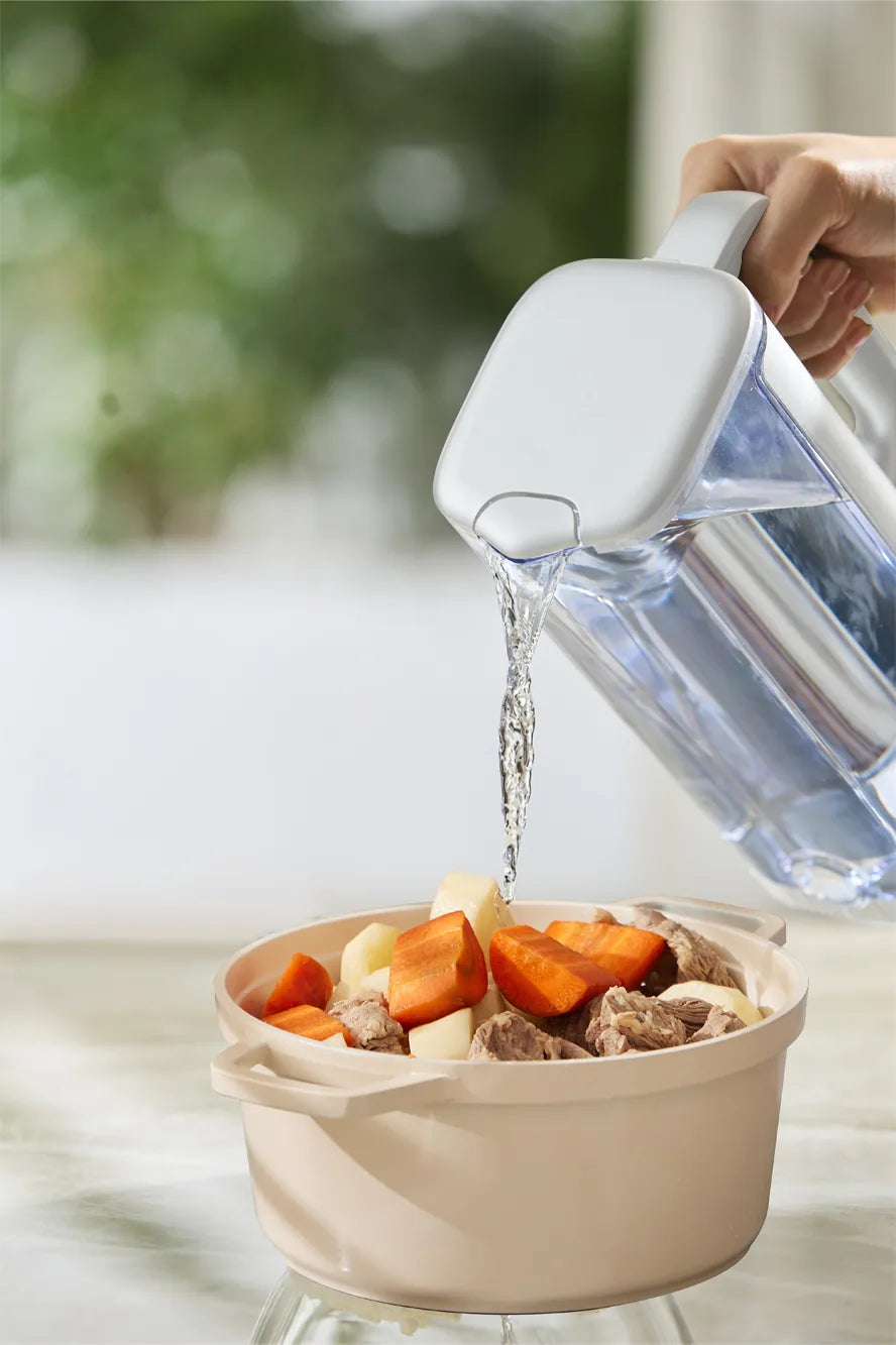 Hand pouring filtered water from the Philips jug into a pot of beef, carrots, and potatoes.