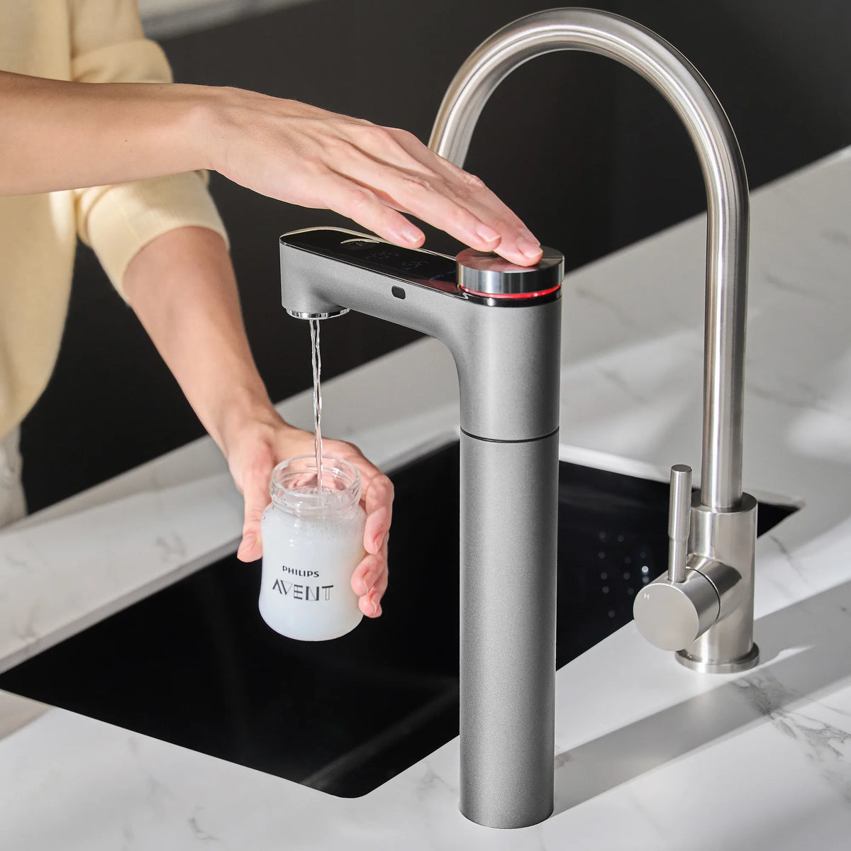 Hand over the Philips RO tap's knob as hot water fills a Philips Avent baby bottle at a kitchen sink.