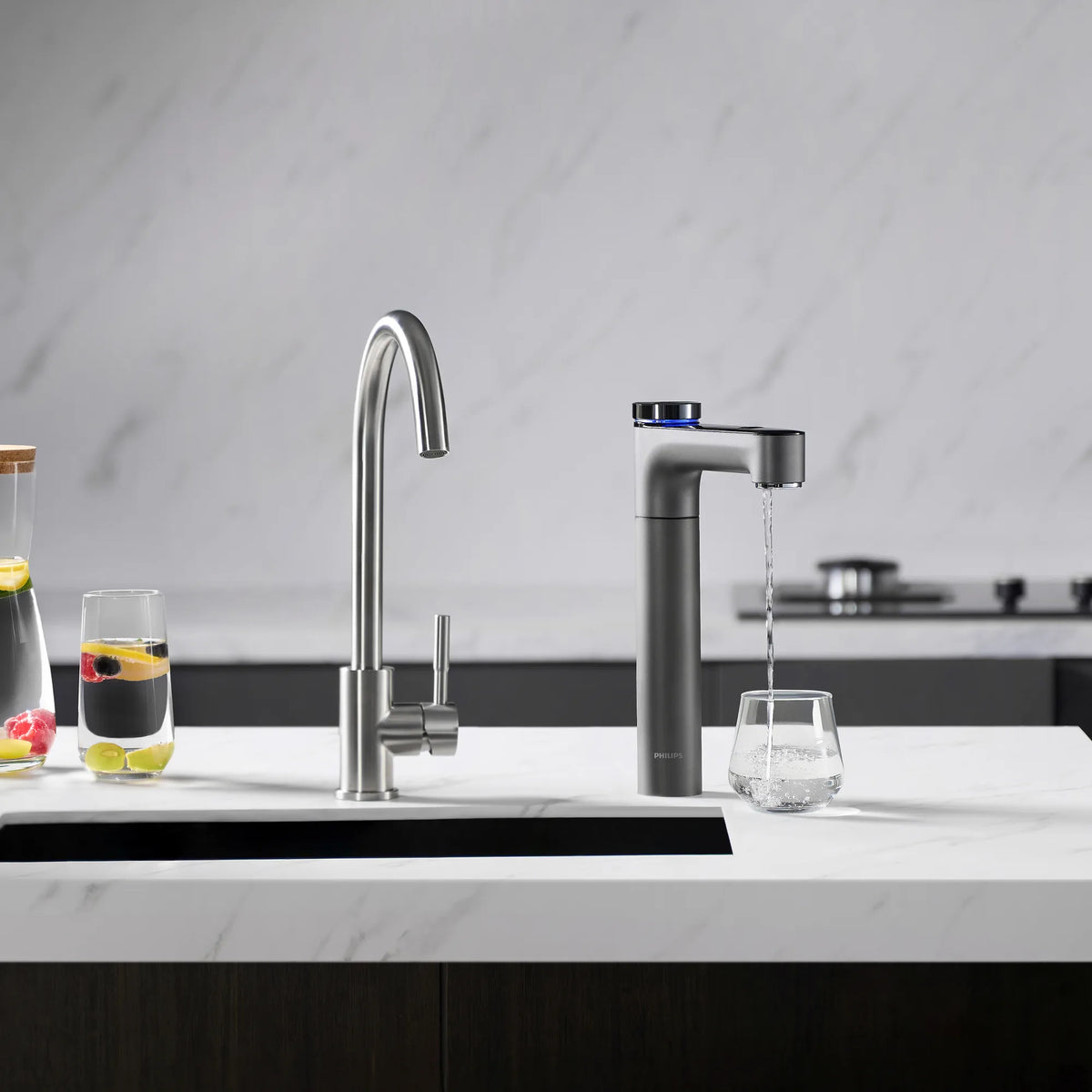 Philips RO tap dispensing chilled water into a glass, beside a stainless steel faucet and glasses of fruit-infused water.