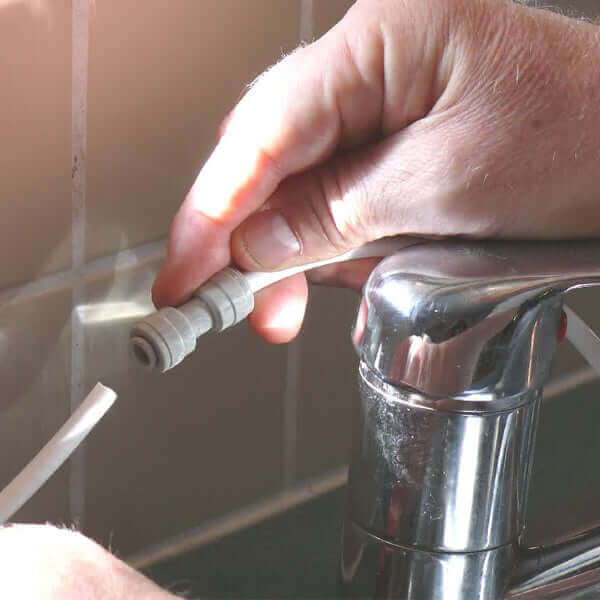 Hands connecting the 3 Stage Portable Reverse Osmosis Water Filter System to a faucet in a tiled kitchen.
