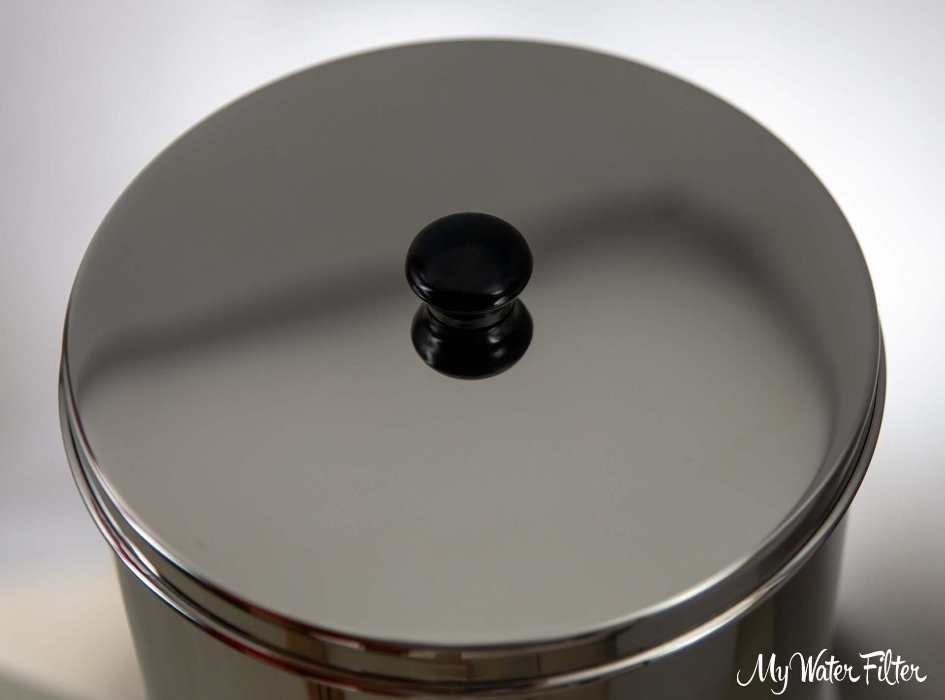A close up of Phoenix lid made from stainless steel, featuring a light-reflective surface and a black handle.