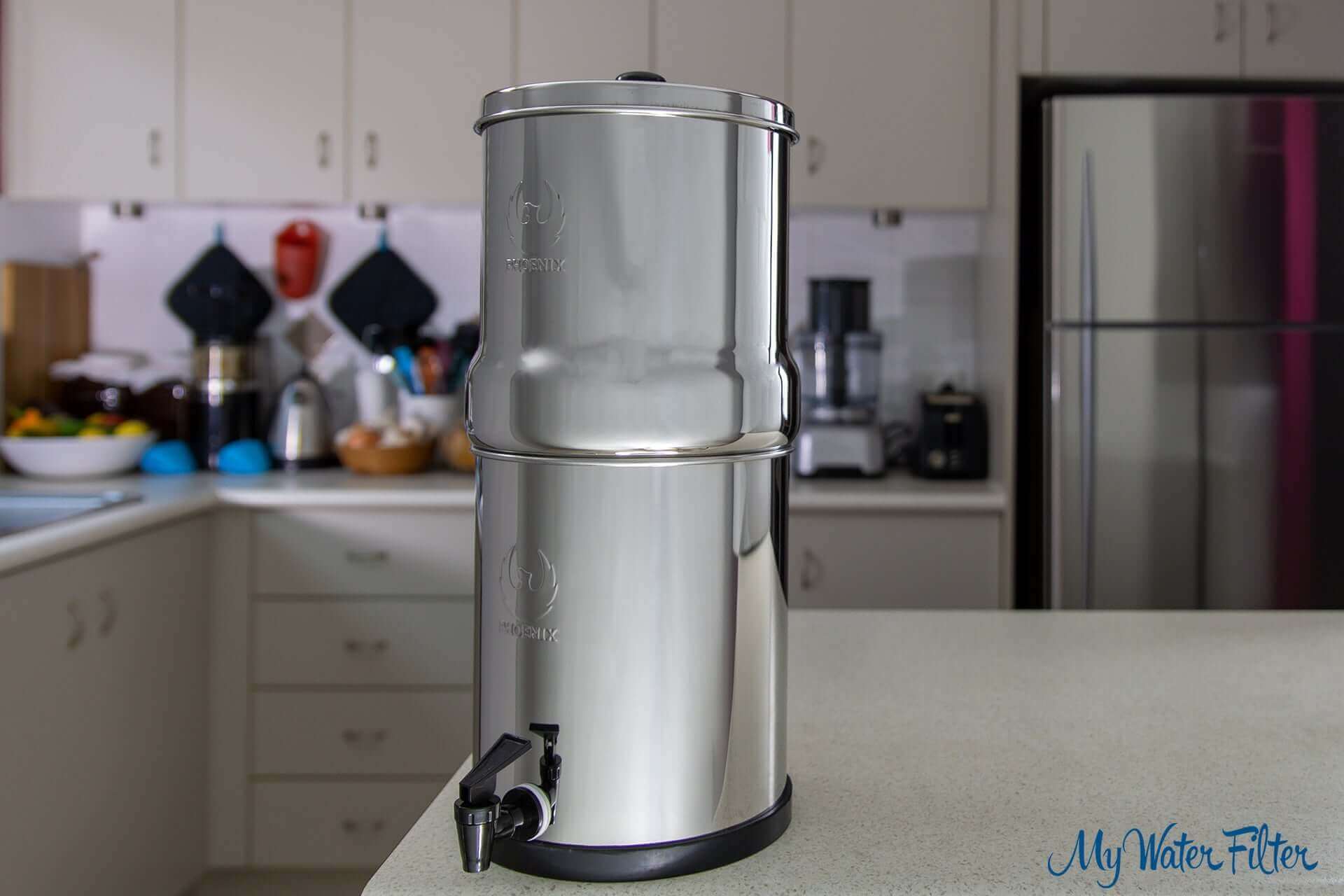 Phoenix Stainless Steel Gravity Water Filter on a kitchen counter with cabinets in the background.