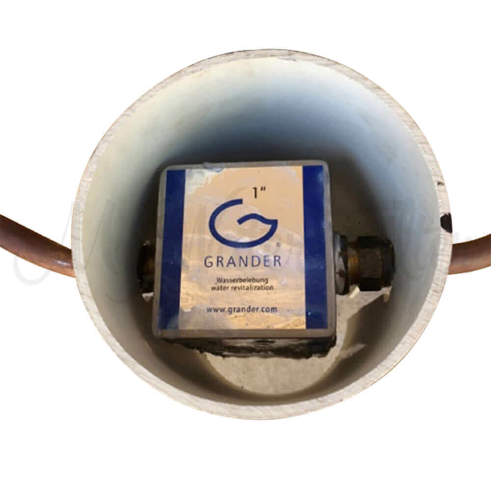 A Grander Whole House System, a water revitalization device by Grander, is installed inside a cover with a pipe.