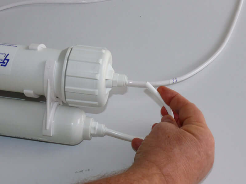 Hand connecting white tubing to 3 Stage Portable Reverse Osmosis Water Filter System on gray surface.