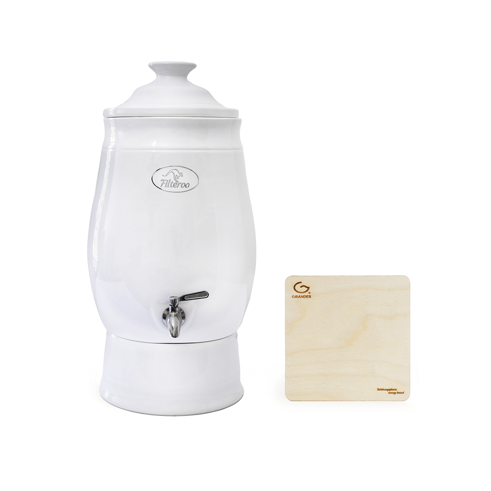 A Filteroo® Joey 12L Gravity Ceramic Water Filter with Grander Revitalised Structured Water, featuring a spout, stands beside a light wooden plaque displaying the Filteroo brand logo and text.