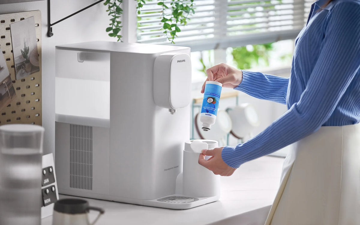 Woman in a blue knit sweater inserting the coconut shell carbon filter into the side of a white Philips water station on a kitchen counter.