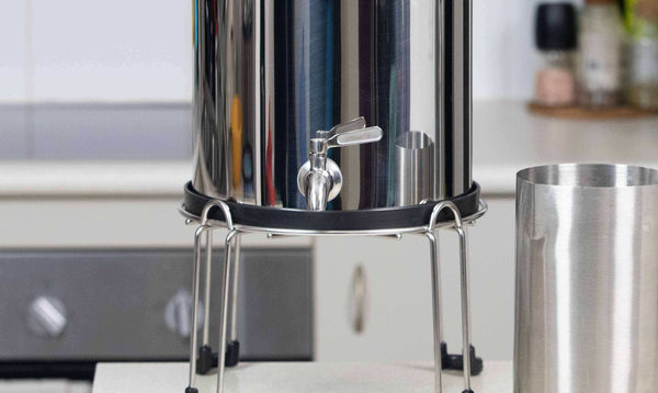 Filteroo® Superoo stainless steel gravity water filter on a stand featuring the stainless steel tap and jug in a kitchen setting.