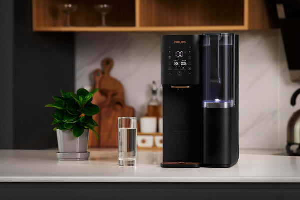 Philips Aquaporin Reverse Osmosis Water Station ADD6920BK/79, black, on kitchen counter with water glass and plant.