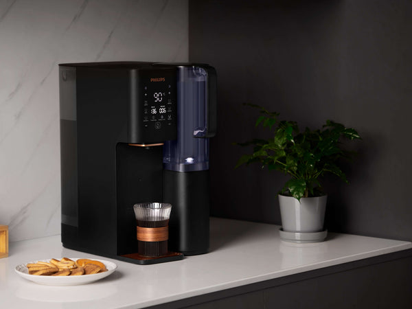 Philips Aquaporin Water Station ADD6920BK/79 on kitchen counter with plant and cookies.