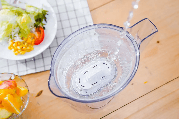 A top view of Philips Micro X-Clean Carbon Filter is being used to pour water into a pitcher on a table with salad and fruit nearby.