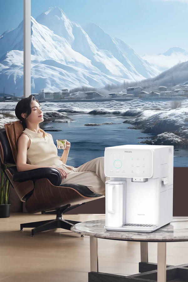 Woman relaxing in a lounge chair with a drink, beside the white Philips water station, with a snowy mountain view behind.