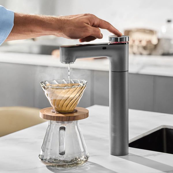 Hand pressing the knob on the Philips RO tap as hot water pours over coffee grounds in a glass pour-over dripper.