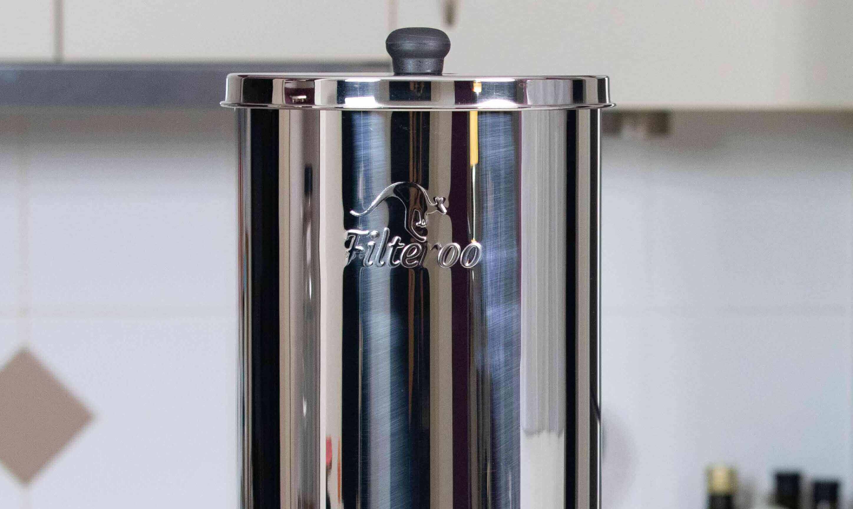 Close-up of a stainless steel container with a black lid knob, branded Filteroo® Superoo, in a kitchen setting.