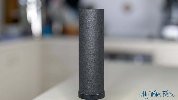 A black cylindrical Phoenix carbon block filter cartridge sits on a kitchen counter.