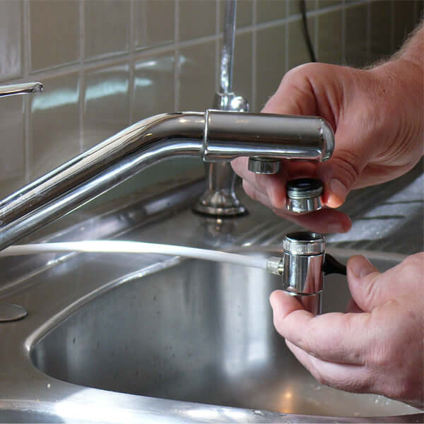 An individual skillfully disassembles a kitchen faucet above a stainless steel sink, preparing to install the 3 Stage Portable Reverse Osmosis Water Filter System, designed to remove fluoride.