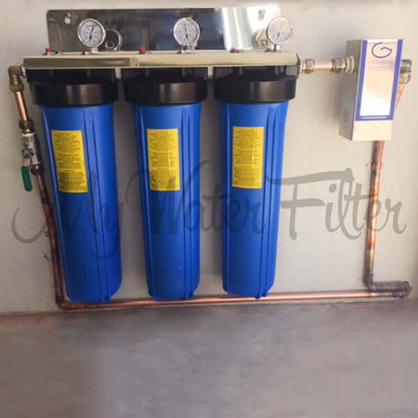 Fully installed MWF 20" x 4.5" Triple Big Blue Whole House Water Filter System, featuring a stainless steel bracket, 3 pressure gauges, 3 blue housings with black head caps, a Grander Whole House Unit on the right copper pipes with valve for a complete setup that mounts neatly on the wall.